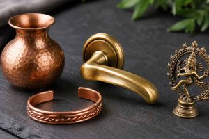 Collection d'objets en cuivre et laiton sur une surface en ardoise : vase décoratif, poignée de porte, bracelet en cuivre et petite figurine en bronze. Guide d'entretien selon le type d'objet